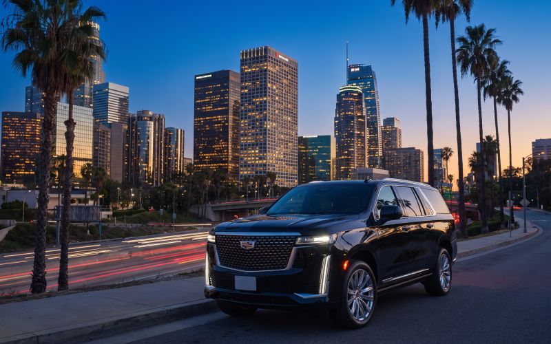 Black Cadillac Escalade parked above a freeway with a downtown skyline at blue hour