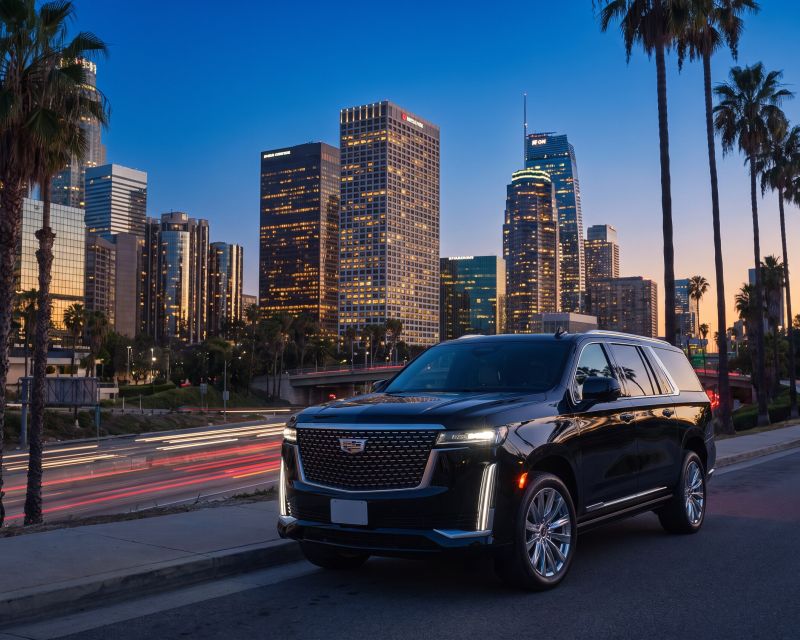 Black Cadillac Escalade parked above a freeway with a downtown skyline at blue hour