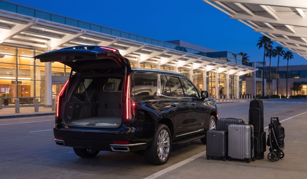 Suitcases, a golf travel bag and a folded stroller on the curb beside the open rear of the Black Cadillac Escalade