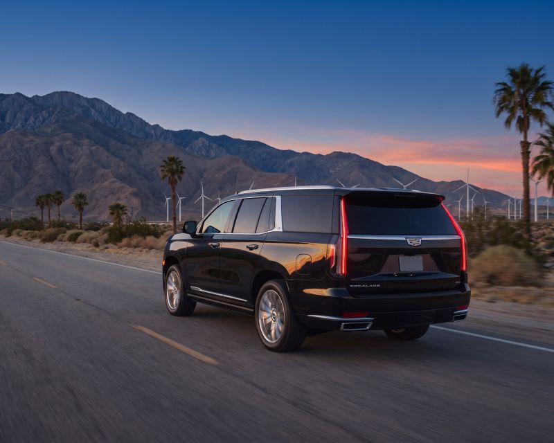 Black Cadillac Escalade on a desert highway with wind turbines and mountains at dusk